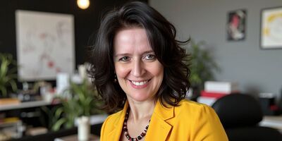 Nicole Angela Buck – KI-Trainerin und Kommunikationsdesignerin in ihrem Atelier, lächelnd in gelbem Blazer